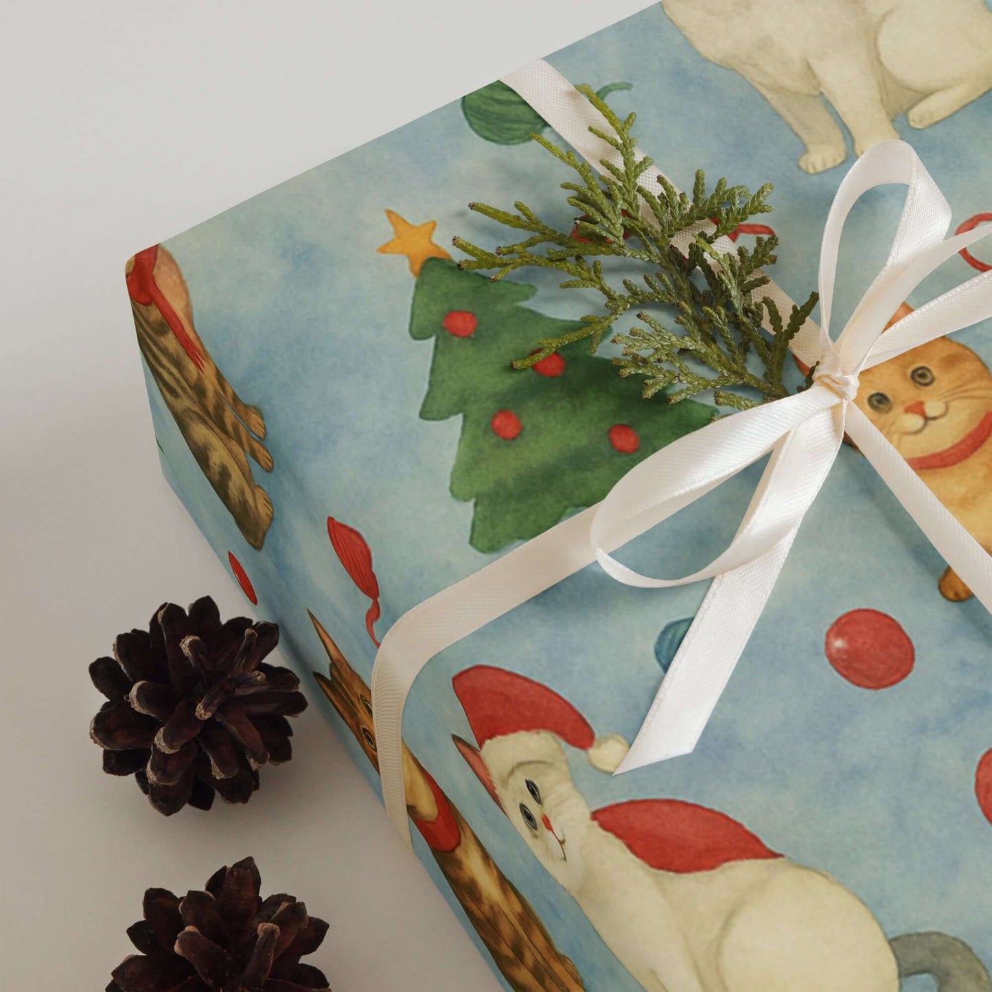 Luxury Christmas wrapping paper featuring whimsical watercolor cats, festive trees, and ornaments, tied with a ribbon.