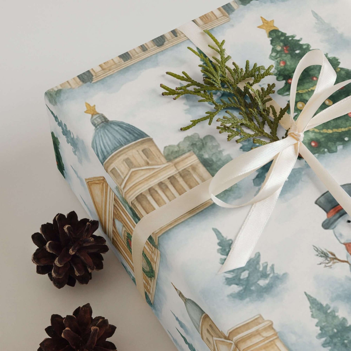 Luxury Christmas wrapping paper featuring watercolor seasonal landmarks, topped with greenery and pinecones.
