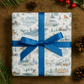 Luxury Iceland Christmas wrapping paper featuring watercolor designs of landscapes and village scenes, tied with a blue ribbon.