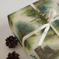 Luxury Christmas wrapping paper featuring watercolor wilderness scenes with boots, pinecones, and greenery.