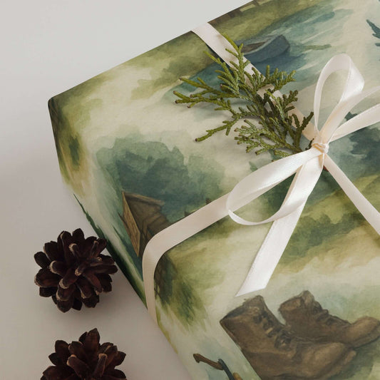Luxury Christmas wrapping paper featuring watercolor wilderness scenes with boots, pinecones, and greenery.