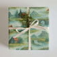 Iceland Wrapping Paper featuring hand-painted landscapes of waterfalls and Icelandic cottages, beautifully tied with a ribbon.