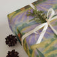 Luxury Christmas wrapping paper featuring watercolor lavender fields and rustic barns, styled with pinecones and greenery.