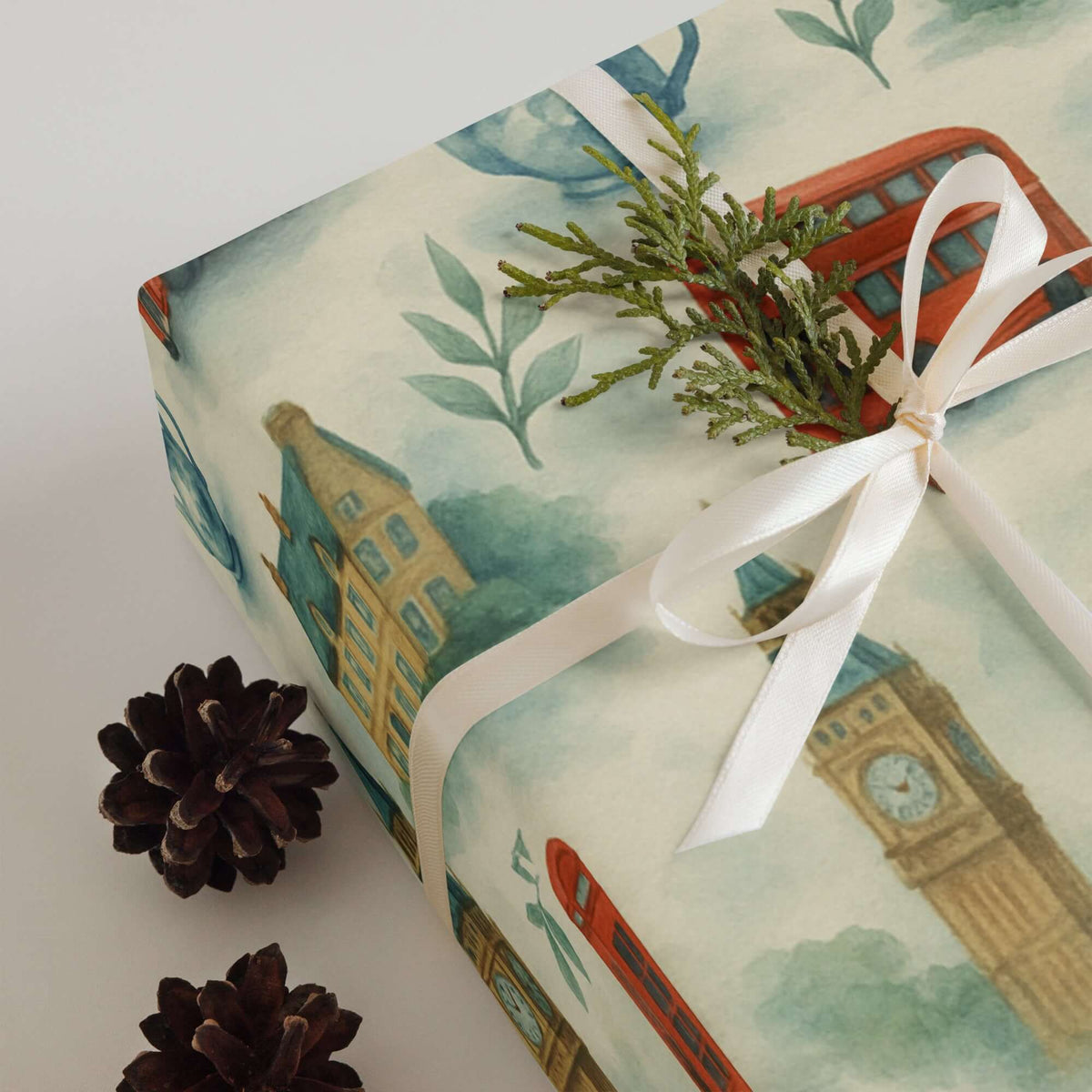 London Tea Wrapping Paper featuring Big Ben and red buses, accented with greenery and pinecones.