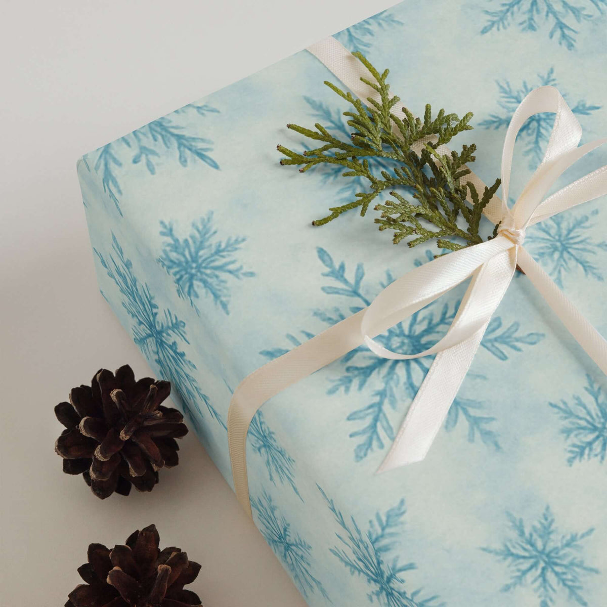 Snowflakes Christmas Wrapping Paper adorned with greenery and pine cones for a festive holiday gift.
