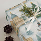 Luxury Christmas wrapping paper featuring watercolor seasonal landmarks, topped with greenery and pinecones.