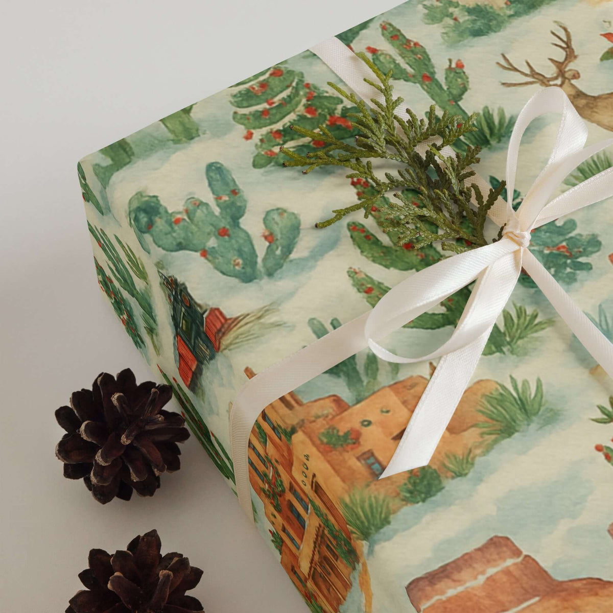 Luxury Southwest USA Christmas wrapping paper with watercolor desert scenes and festive decorations, styled with pinecones.