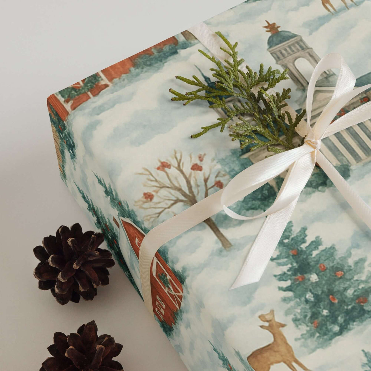 Luxury Christmas wrapping paper featuring a watercolor snowy scene with rustic barns and pine accents.