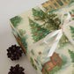 Luxury Christmas wrapping paper showcasing a watercolor design of a snowy village with pine accents and festive colors.