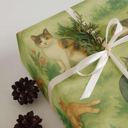 Cats Wrapping Paper featuring adorable cat illustrations among greenery and a decorative bow with pinecones.