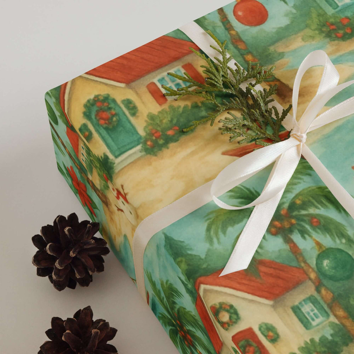 Caribbean Tropical Christmas Wrapping Paper on a gift box adorned with greenery and feminine ribbon, pine cones nearby.